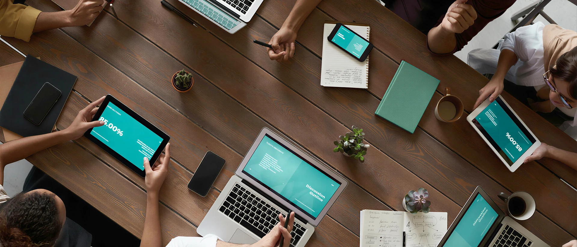 Overhead view of a team around a shared table, laptops, tablets and phones all showing the same presentation
